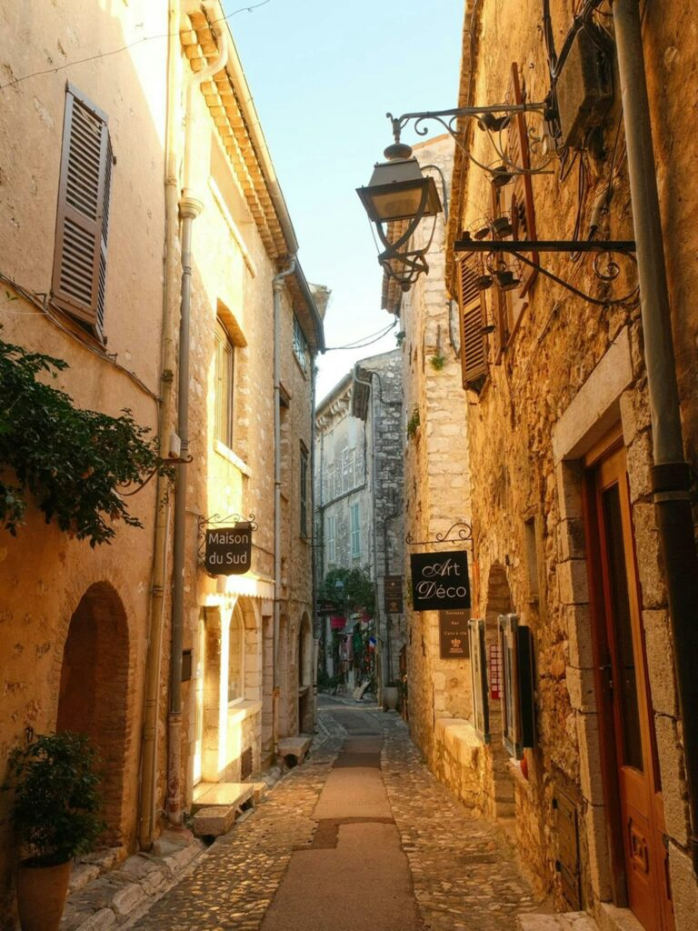 Sunlit narrow street in a picturesque Mediterranean village with stone buildings.