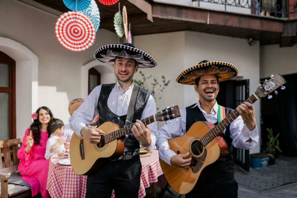 Festive mariachi band playing guitars at a colorful outdoor gathering.